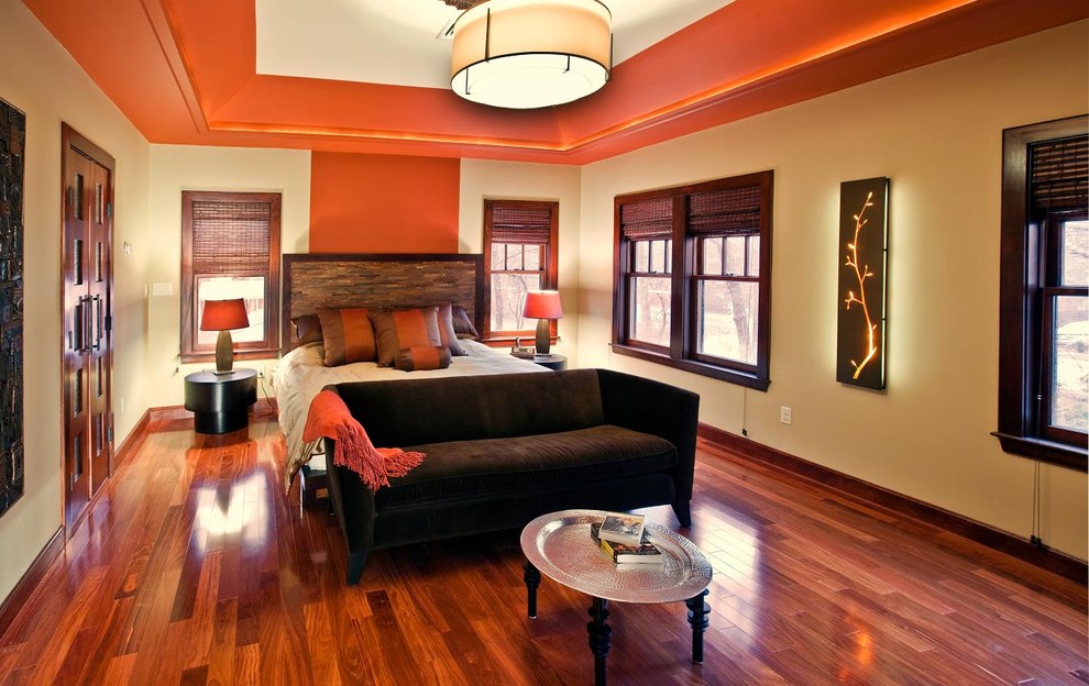 Modelo de dormitorio principal asiático grande con paredes beige, suelo de madera en tonos medios y suelo naranja