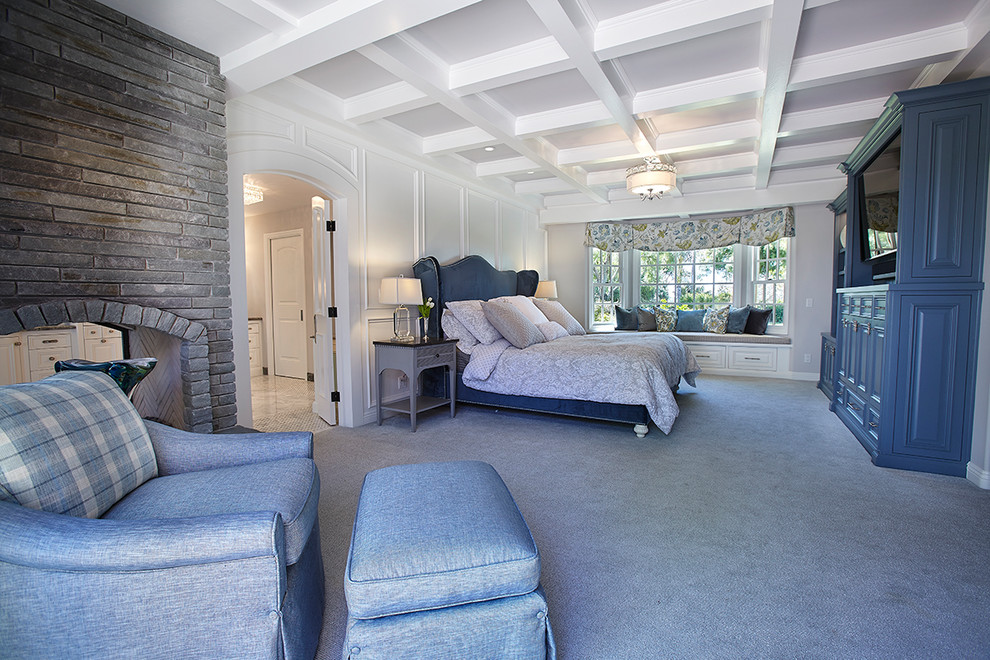Modelo de dormitorio principal tradicional renovado grande con paredes grises, moqueta, chimenea de doble cara, marco de chimenea de piedra y suelo gris