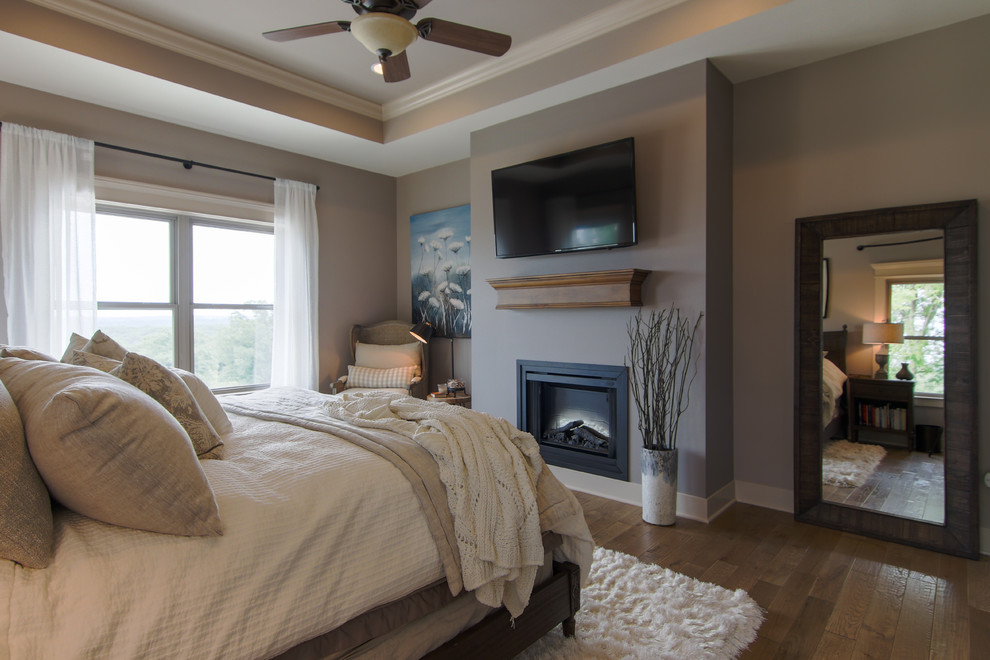 Großes Rustikales Hauptschlafzimmer mit grauer Wandfarbe, braunem Holzboden, Kamin, Kaminumrandung aus Holz und braunem Boden in Sonstige