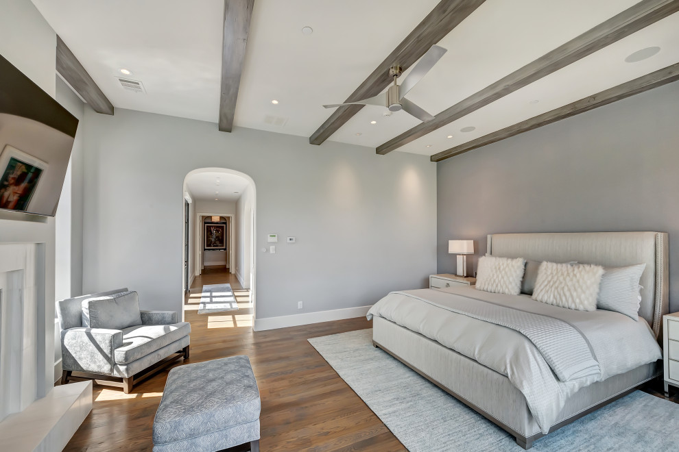 Inspiration for a large mediterranean master bedroom in Dallas with grey walls, medium hardwood flooring, a standard fireplace, a stone fireplace surround and brown floors.