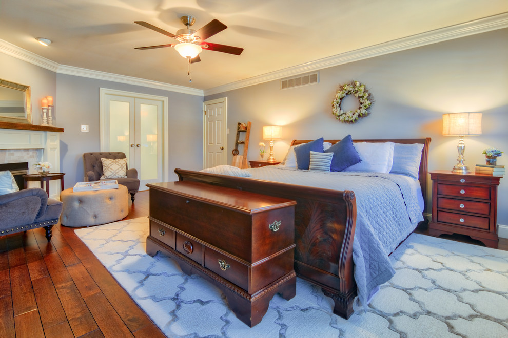 Exemple d'une grande chambre parentale chic avec un mur bleu, un sol en bois brun, une cheminée standard, un manteau de cheminée en métal et un sol marron.