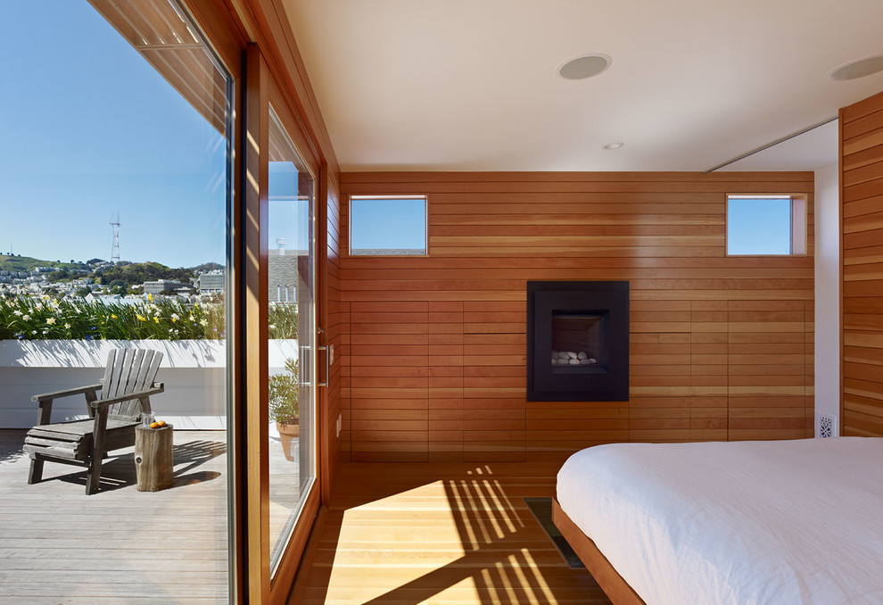 Esempio di una grande camera da letto stile loft minimalista con pavimento in legno massello medio, cornice del camino in metallo e camino classico