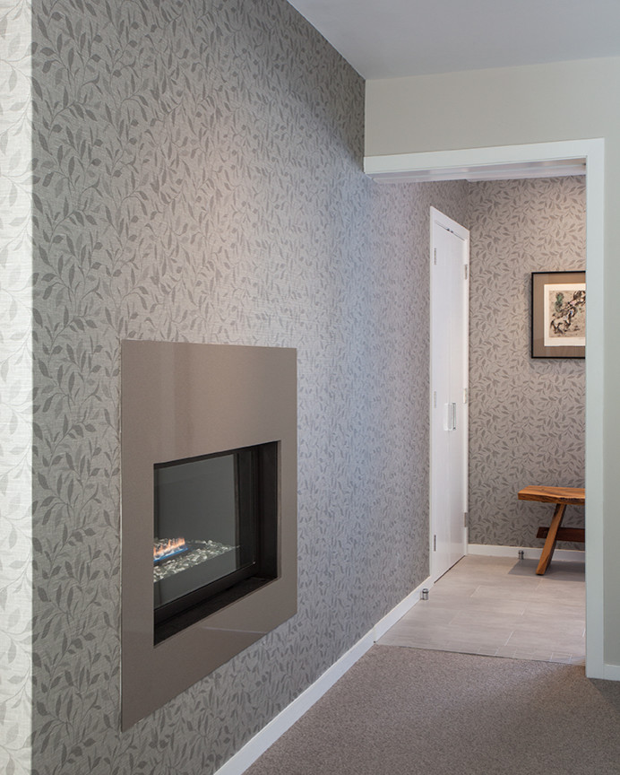 Réalisation d'une grande chambre avec moquette marine avec un mur gris, une cheminée ribbon et un manteau de cheminée en pierre.