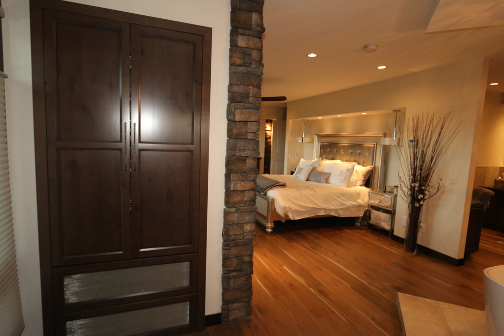 Modelo de dormitorio principal rústico extra grande con paredes blancas, suelo de madera clara, chimenea de esquina y marco de chimenea de piedra