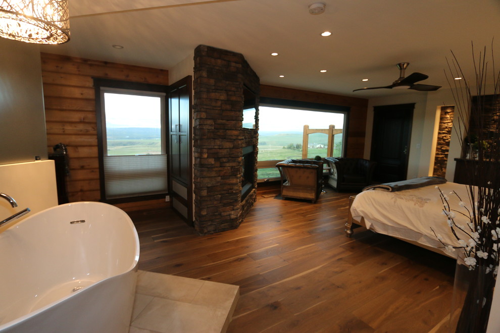 Ejemplo de dormitorio principal rural extra grande con paredes blancas, suelo de madera clara, chimenea de esquina y marco de chimenea de piedra