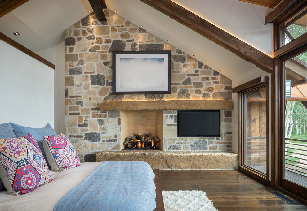 Inspiration for a rustic bedroom in Denver with beige walls, dark hardwood flooring, a standard fireplace, a stone fireplace surround and a feature wall.