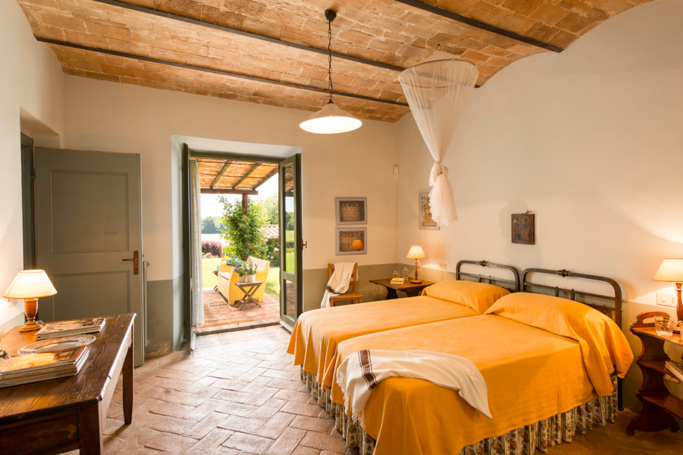 Esempio di una camera degli ospiti mediterranea di medie dimensioni con pareti bianche e pavimento in mattoni