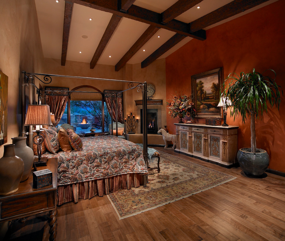 Mediterranes Schlafzimmer mit oranger Wandfarbe, braunem Holzboden und Eckkamin in Sonstige