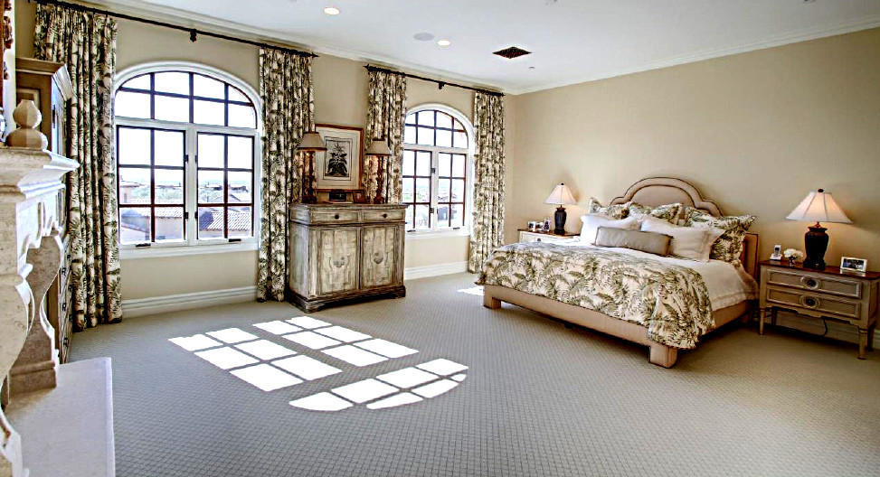 На фото: большая хозяйская спальня в средиземноморском стиле с бежевыми стенами, ковровым покрытием, горизонтальным камином, фасадом камина из камня и бежевым полом