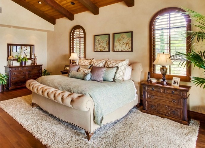 Expansive mediterranean master bedroom in San Diego with beige walls, dark hardwood flooring, a standard fireplace, a stone fireplace surround and brown floors.