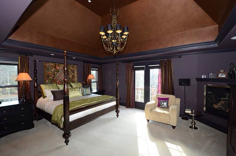 На фото: большая хозяйская спальня в классическом стиле с фиолетовыми стенами, ковровым покрытием, угловым камином и фасадом камина из дерева