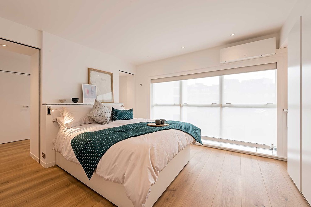 Imagen de dormitorio actual de tamaño medio sin chimenea con paredes blancas y suelo de madera clara