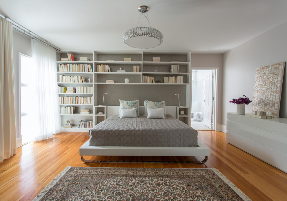 Cette image montre une grande chambre parentale design avec un mur gris, un sol en bois brun, aucune cheminée et un sol marron.