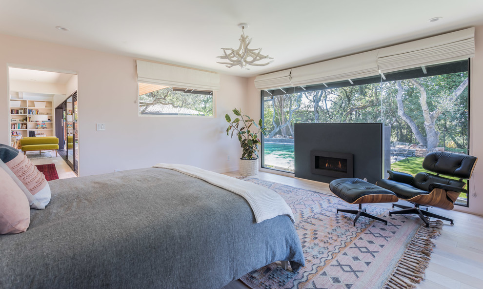 Modelo de dormitorio principal vintage con paredes blancas, suelo de madera clara, chimenea lineal, marco de chimenea de hormigón y suelo beige
