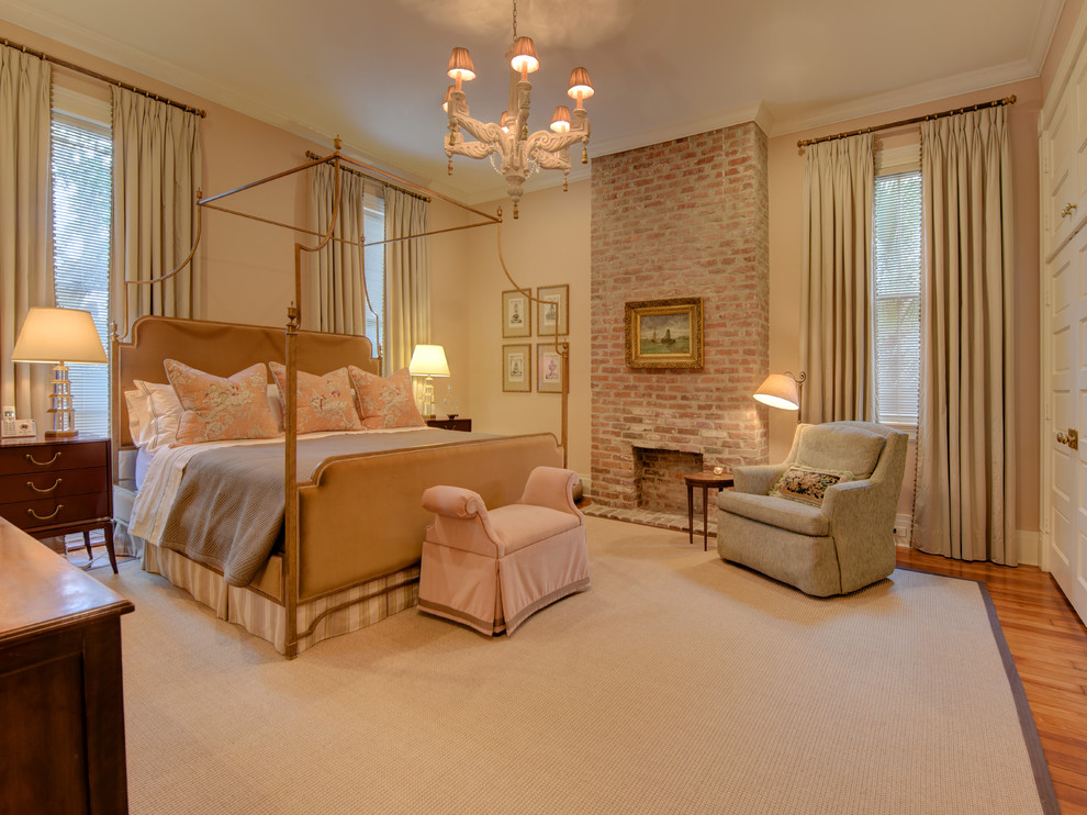 This is an example of a large classic master bedroom in New Orleans with beige walls, medium hardwood flooring, a standard fireplace, a brick fireplace surround and brown floors.