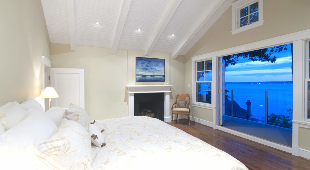 Imagen de dormitorio costero de tamaño medio con paredes beige, suelo de madera en tonos medios, todas las chimeneas y marco de chimenea de madera