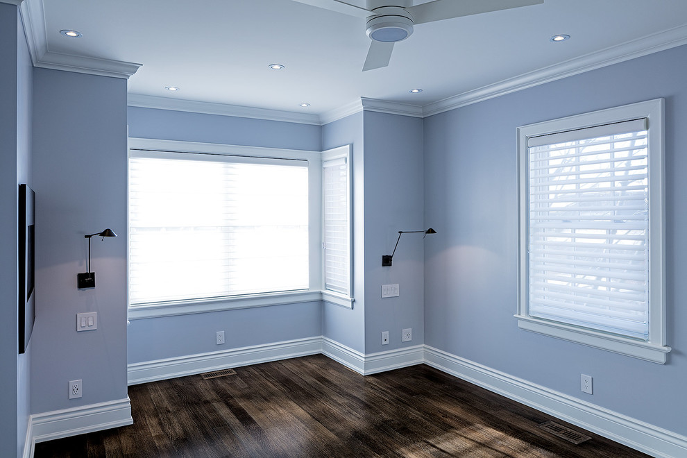 Modelo de dormitorio principal clásico pequeño con paredes azules, suelo de madera en tonos medios, chimenea de doble cara y marco de chimenea de yeso