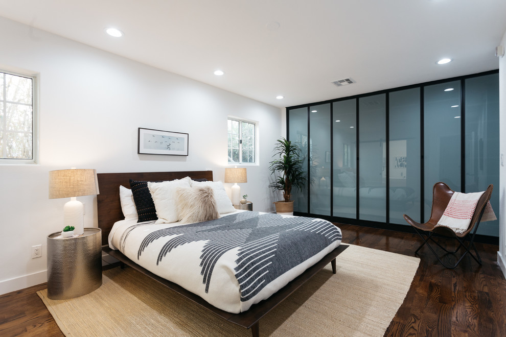 Cette image montre une chambre design avec un mur blanc, parquet foncé et un sol marron.