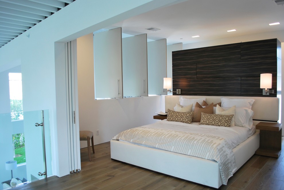 Modelo de dormitorio principal minimalista grande con paredes blancas y suelo de madera en tonos medios