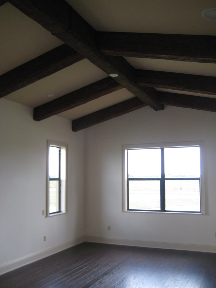 Modelo de dormitorio principal rústico de tamaño medio sin chimenea con paredes blancas, suelo de madera oscura y suelo marrón