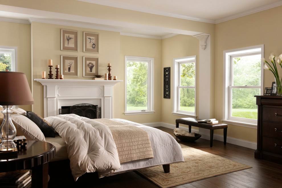 This is an example of a medium sized traditional master bedroom in Orange County with yellow walls, dark hardwood flooring, a standard fireplace, brown floors and a chimney breast.