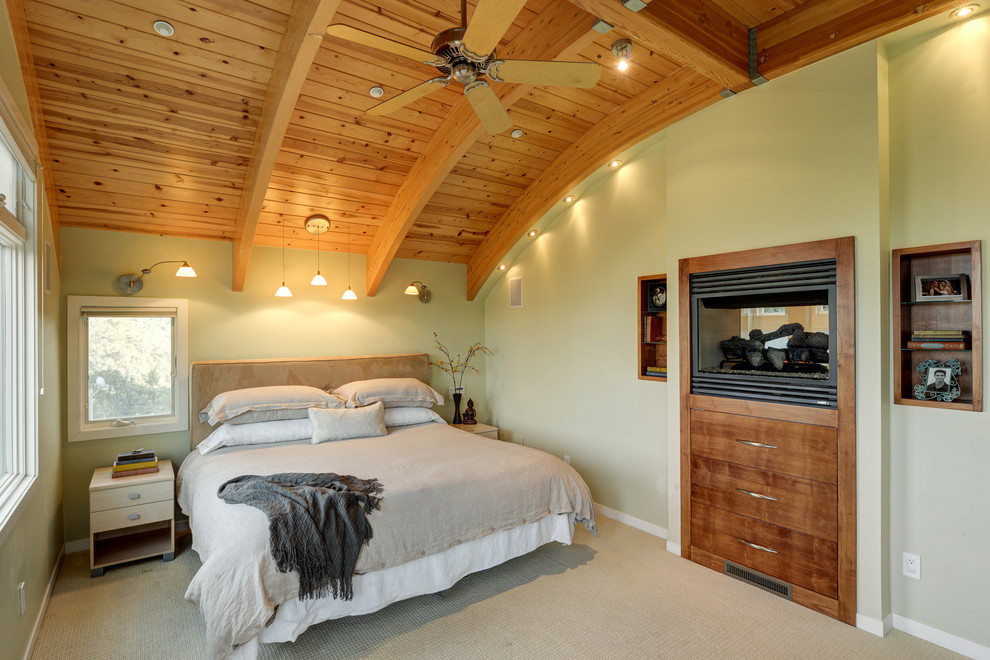 Пример оригинального дизайна: хозяйская спальня среднего размера в современном стиле с зелеными стенами, ковровым покрытием, двусторонним камином и фасадом камина из дерева
