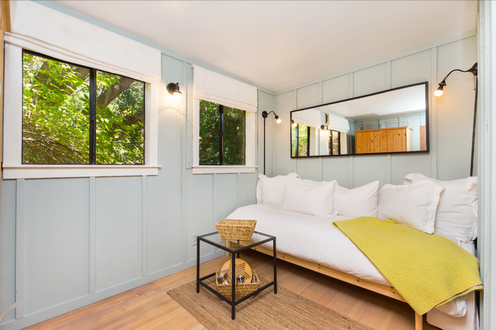 Imagen de habitación de invitados rural pequeña sin chimenea con paredes azules y suelo de madera clara
