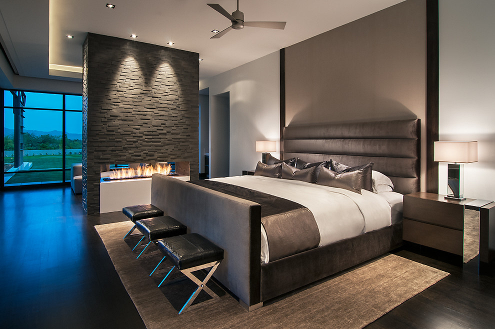 This is an example of a contemporary master bedroom in Phoenix with white walls, dark hardwood flooring, a stone fireplace surround, a two-sided fireplace and feature lighting.