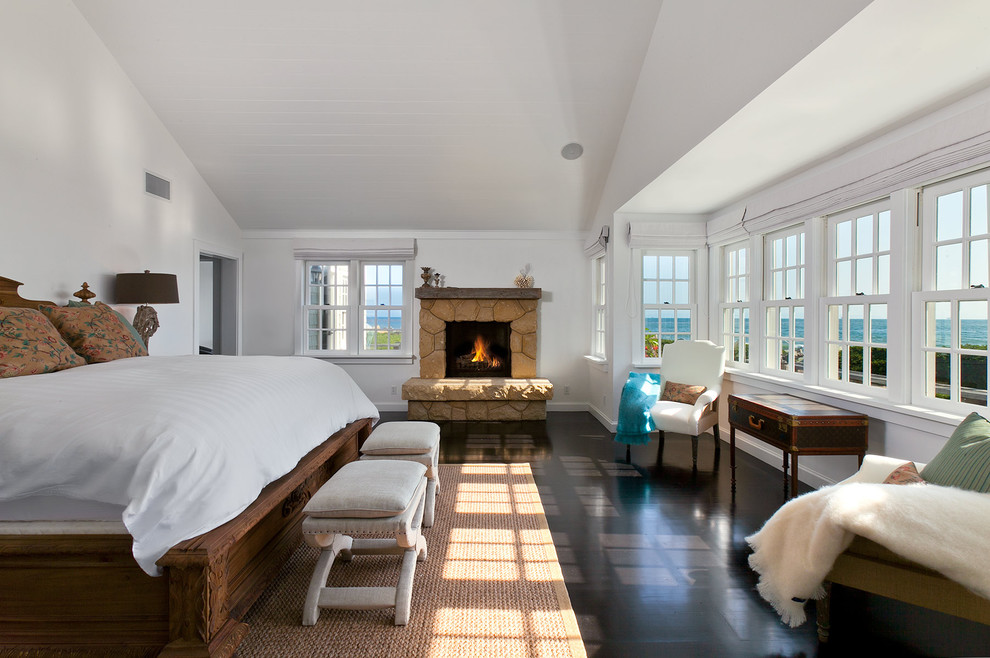 Klassisches Schlafzimmer mit weißer Wandfarbe, dunklem Holzboden, Kamin, Kaminumrandung aus Stein und schwarzem Boden in Santa Barbara