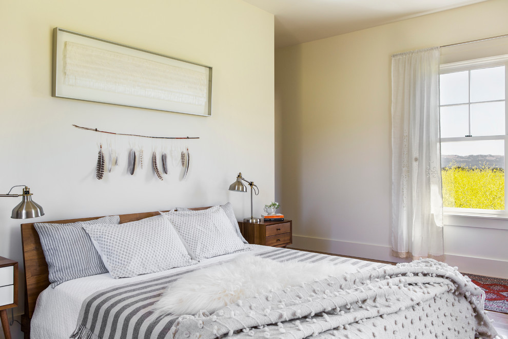 Modelo de dormitorio principal campestre grande sin chimenea con paredes blancas, suelo de madera en tonos medios y suelo marrón