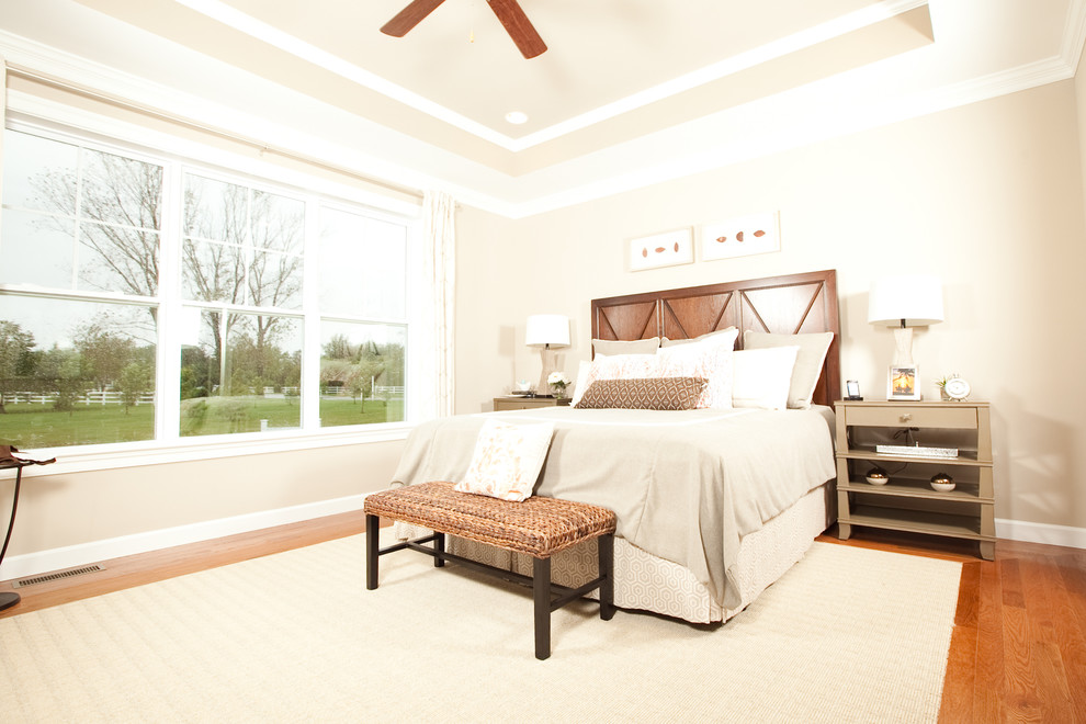 Modelo de dormitorio principal grande sin chimenea con paredes beige y suelo de madera en tonos medios