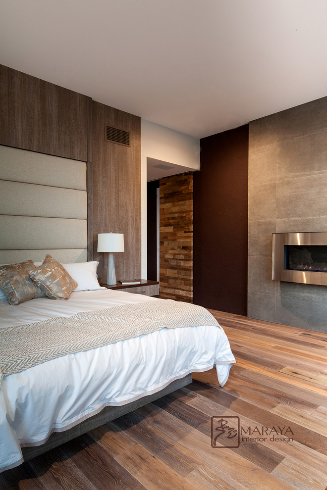 Ejemplo de dormitorio principal actual de tamaño medio con paredes grises, suelo de madera en tonos medios, todas las chimeneas y marco de chimenea de baldosas y/o azulejos