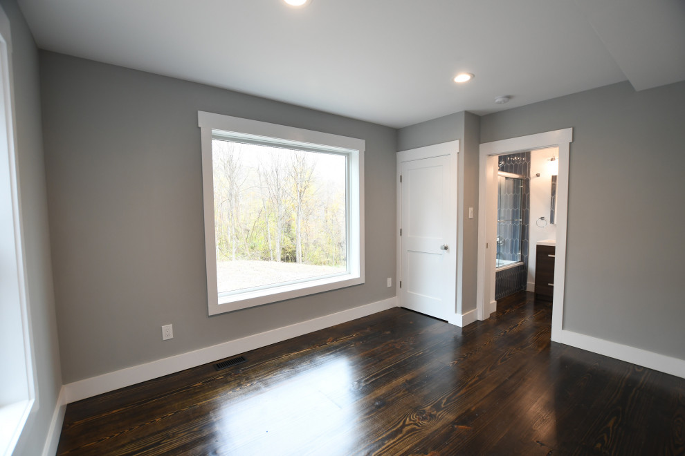 This is an example of a medium sized farmhouse guest bedroom in New York with grey walls, dark hardwood flooring and brown floors.