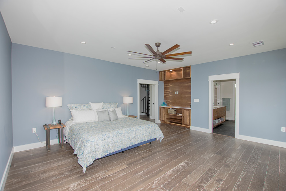 Diseño de dormitorio principal costero grande sin chimenea con paredes azules, suelo de madera en tonos medios y suelo marrón