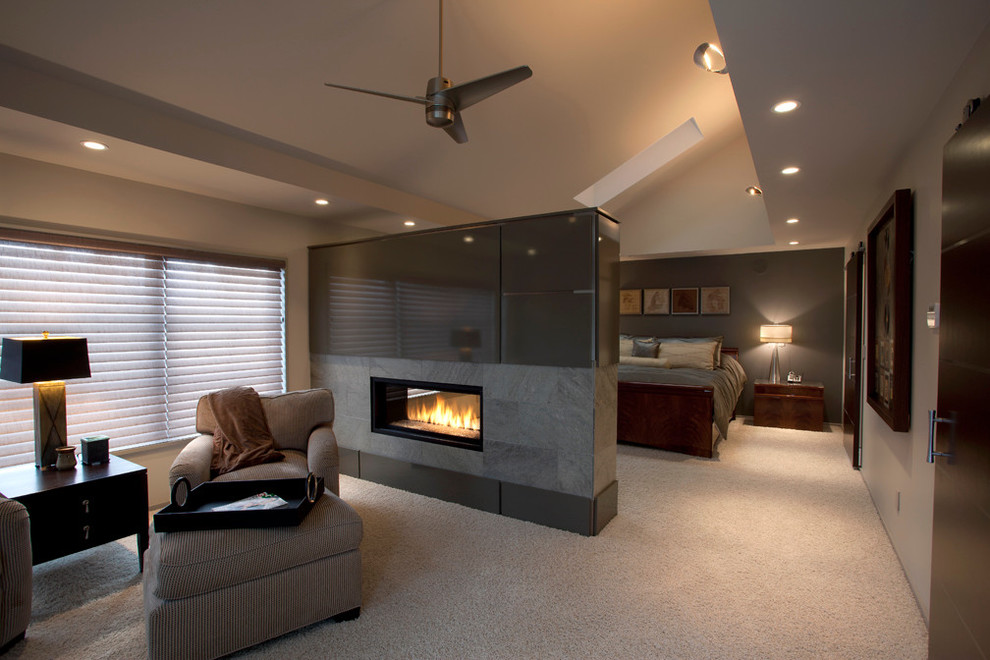 Aménagement d'une grande chambre contemporaine avec un mur gris, une cheminée double-face, un manteau de cheminée en métal et un sol beige.