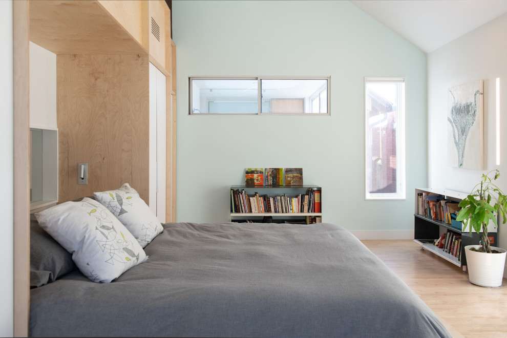 Inredning av ett minimalistiskt sovrum, med blå väggar, ljust trägolv och beiget golv