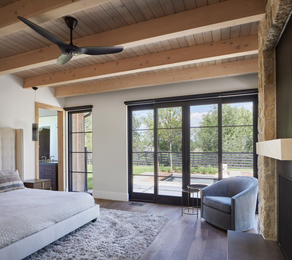 Mittelgroßes Landhausstil Hauptschlafzimmer mit weißer Wandfarbe, braunem Holzboden, Kamin, Kaminumrandung aus Metall, braunem Boden und Holzdecke in Denver