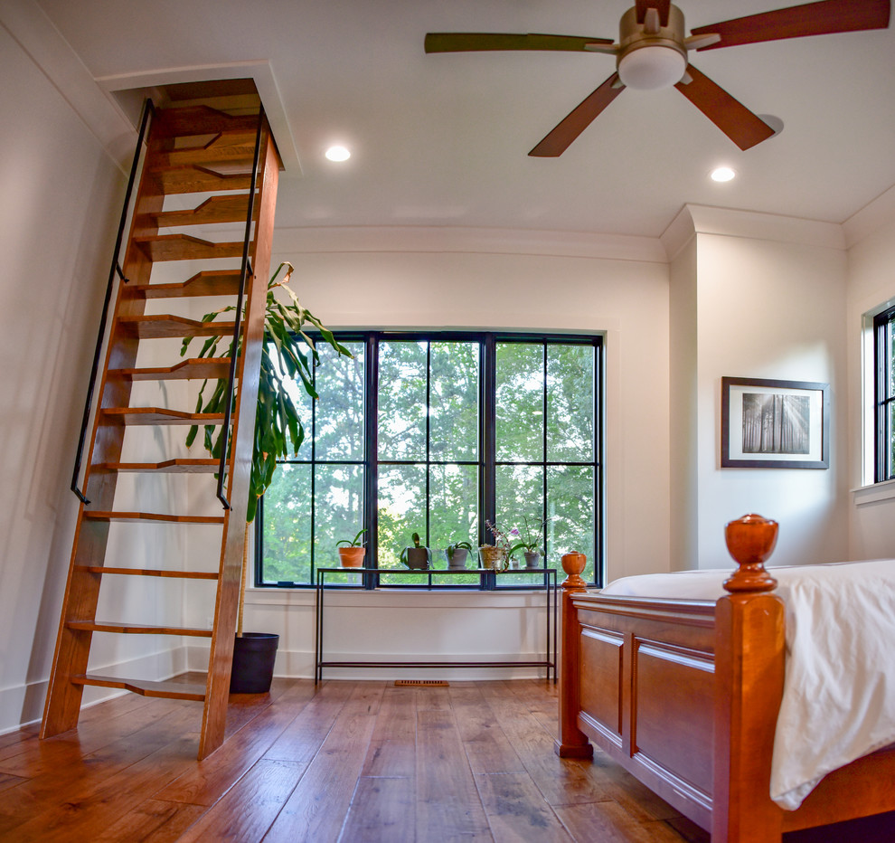Modelo de dormitorio principal de estilo de casa de campo de tamaño medio con paredes blancas, suelo de madera en tonos medios y suelo marrón