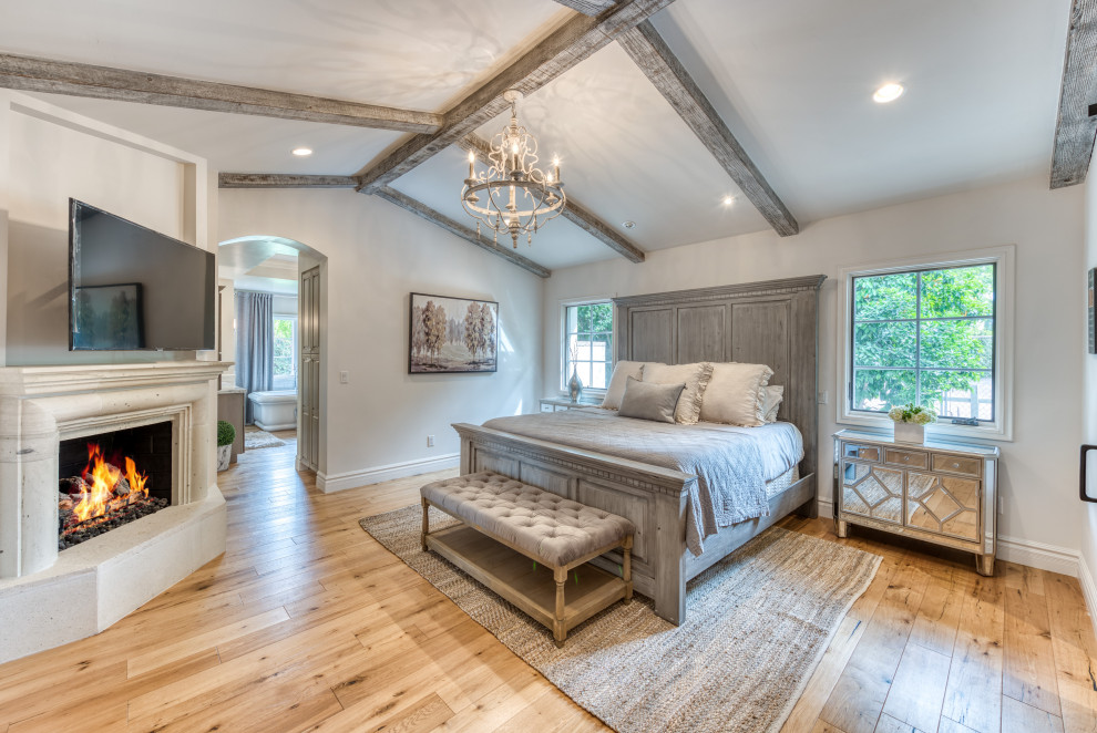 Ejemplo de dormitorio principal y abovedado clásico con paredes blancas, suelo de madera en tonos medios, todas las chimeneas, suelo marrón y vigas vistas
