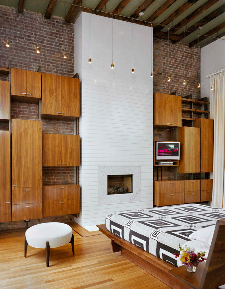 Immagine di una camera da letto design con pareti bianche, pavimento in legno massello medio e camino classico