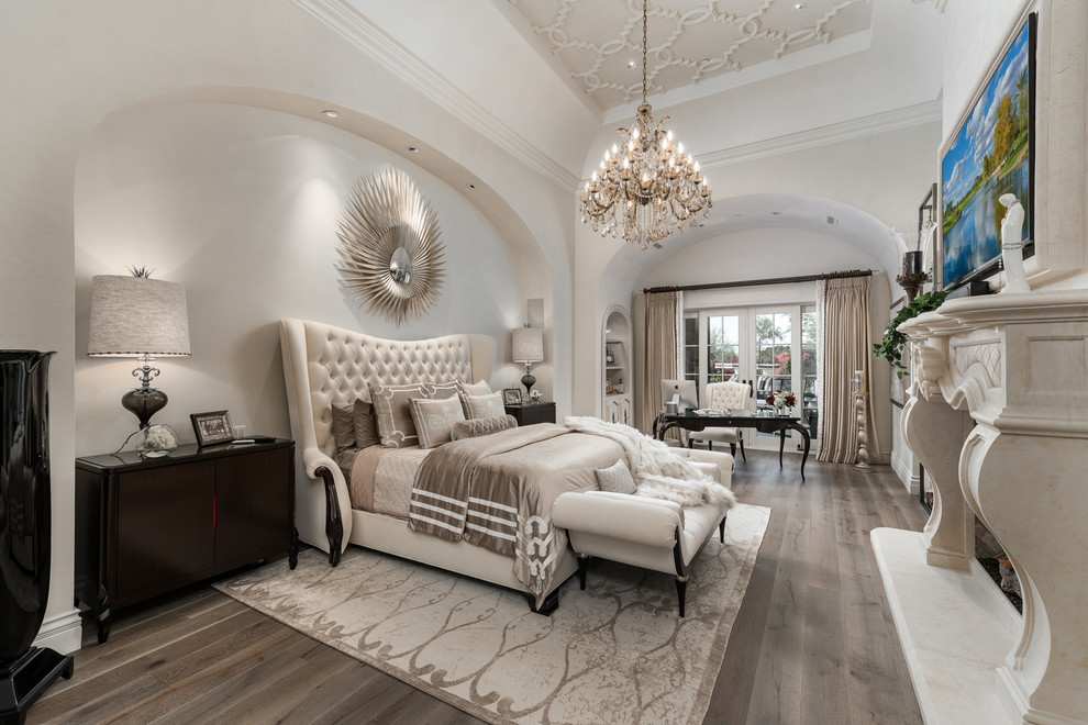 Geräumiges Shabby-Look Hauptschlafzimmer mit weißer Wandfarbe, braunem Holzboden, Tunnelkamin, Kaminumrandung aus Stein und braunem Boden in Phoenix