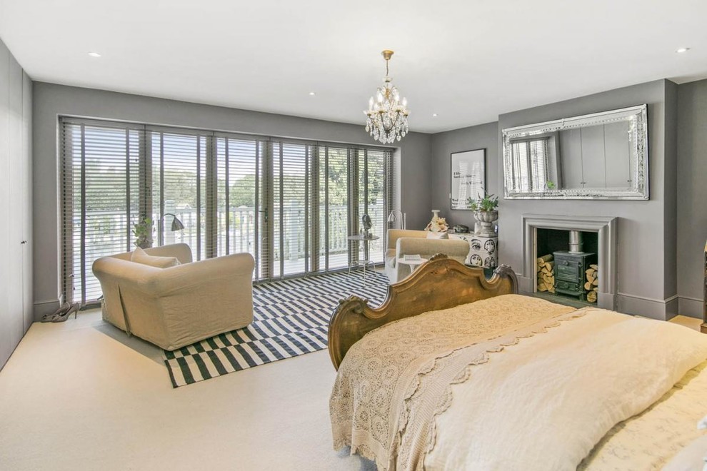 Immagine di una camera da letto classica di medie dimensioni con pareti grigie, moquette, stufa a legna e pavimento beige