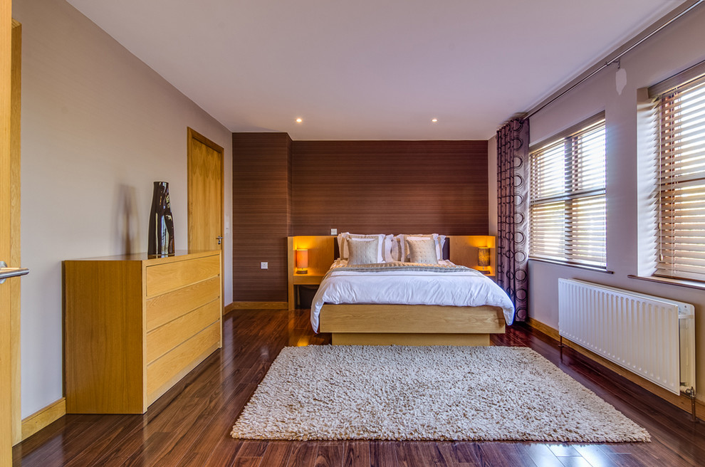 Example of a large minimalist master medium tone wood floor bedroom design in Belfast with beige walls and no fireplace