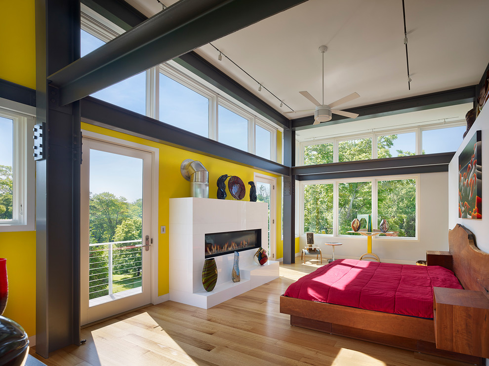 Foto de dormitorio principal actual grande con paredes amarillas, suelo de madera clara, chimenea lineal y marco de chimenea de yeso