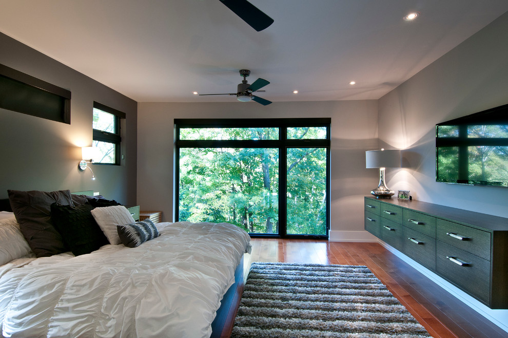Diseño de dormitorio principal actual de tamaño medio sin chimenea con paredes grises y suelo de madera en tonos medios
