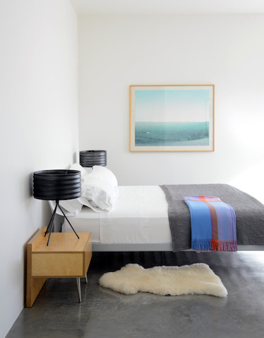 Cette image montre une chambre minimaliste avec un mur blanc, sol en béton ciré et un sol gris.