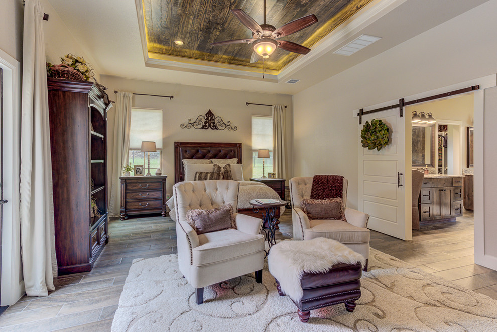 Mittelgroßes Rustikales Hauptschlafzimmer mit beiger Wandfarbe, Porzellan-Bodenfliesen, Kamin, Kaminumrandung aus Stein und braunem Boden in Austin