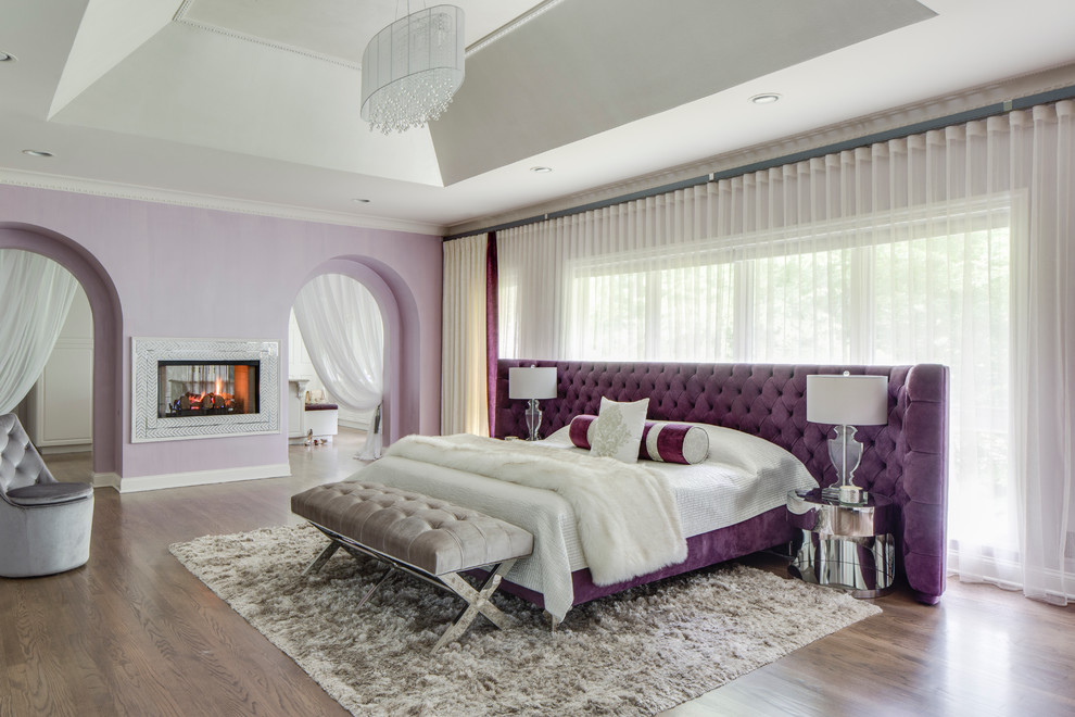 На фото: большая хозяйская спальня в стиле модернизм с фиолетовыми стенами, паркетным полом среднего тона, двусторонним камином и фасадом камина из плитки с