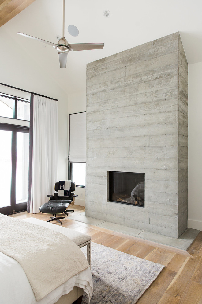 На фото: хозяйская спальня в стиле неоклассика (современная классика) с белыми стенами, светлым паркетным полом, стандартным камином и фасадом камина из бетона