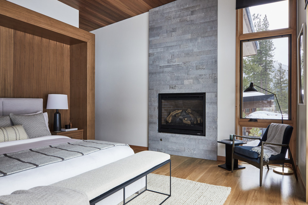 Идея дизайна: спальня в современном стиле с белыми стенами, паркетным полом среднего тона, стандартным камином, фасадом камина из плитки и коричневым полом